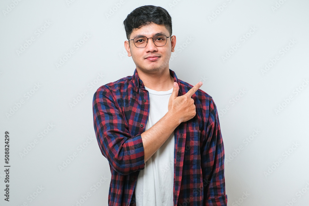 Young handsome asian man pointing with hand finger to the side looking at the camera. Young handsome asian man pointing with hand finger to the side looking at the camera.