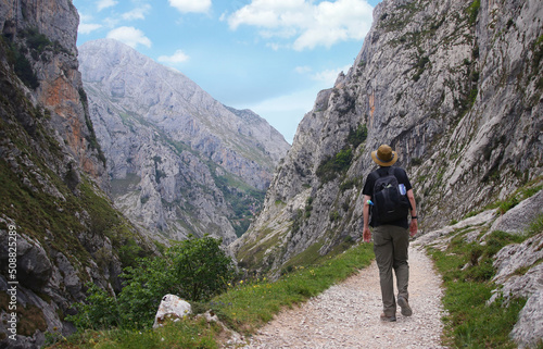Man with a hat at the mountain. Mountaineer walking in the high mountains of Picos de Europa national park. Beautiful mountain landscape with people hiking and trekking outdoors carrying backpacks.. photo