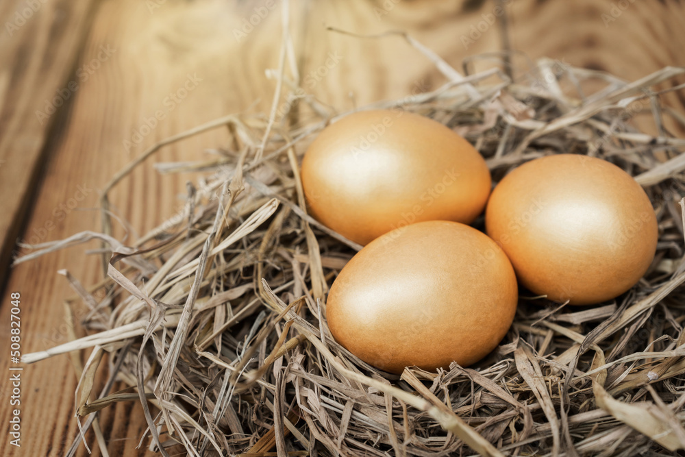 Three golden eggs in a nest of straw with a wooden table background.