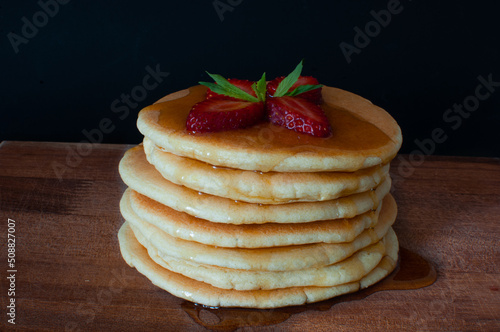 Pancakes with fresh strawberries, maple syrup and mint on wooden plate. Isolated on dark, selective focus.