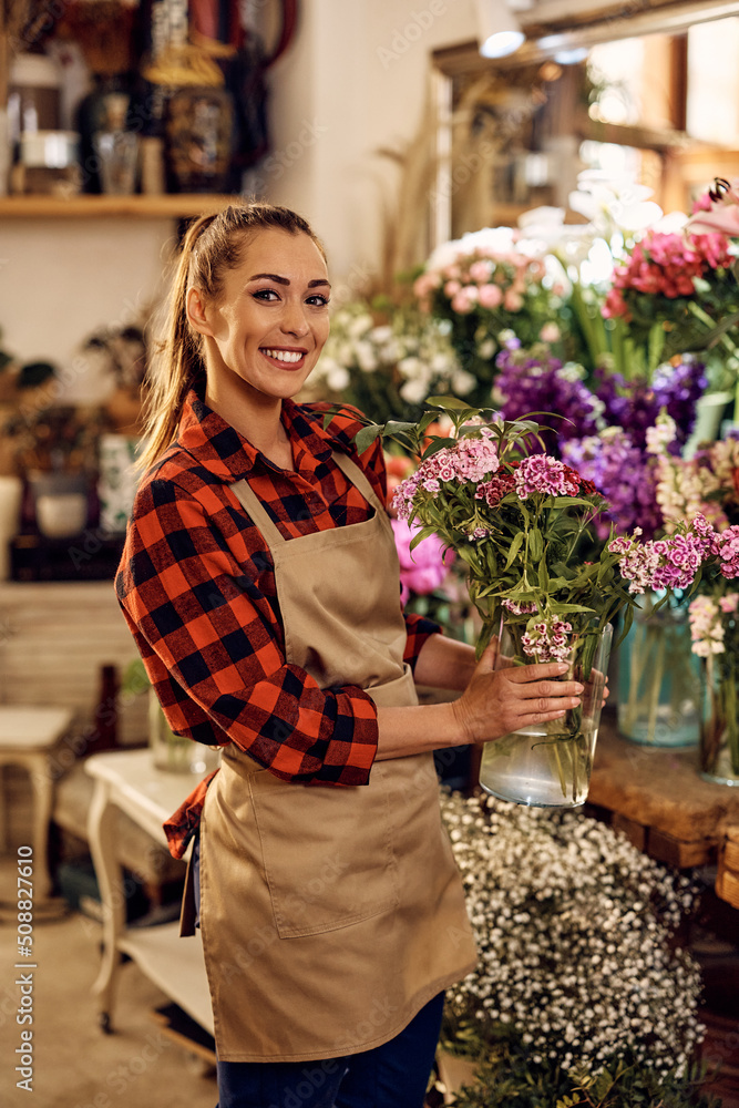 Young happy woman works as florist at flower shop and looking at camera.