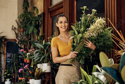 Happy female florist with bouquets at entrance of flower shop looking at camera. photo