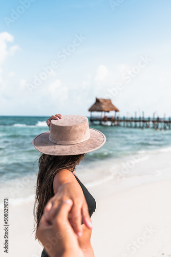 young hispanic woman grabs her partner's hand at the sea - follow me concept