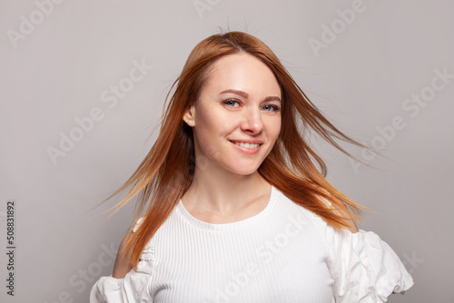Young smiling redhead woman with long smooth blowing glossy frizz hairstyle, beauty portrait