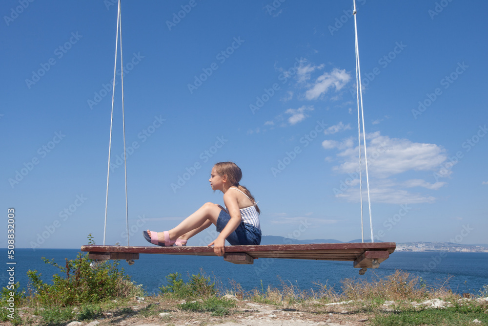 Cute young girl on the playground swing on the sunny summer day