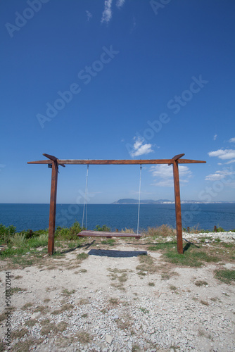 Empty swing in playground with ocean and sky in the background.