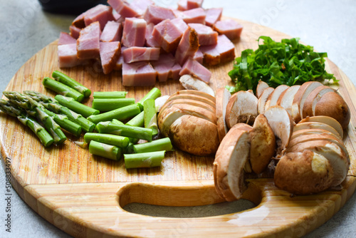 Mushrooms, asparagus and bacon cut on a wooden board.
