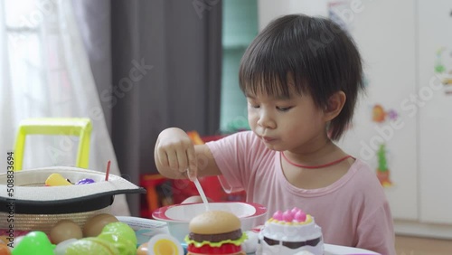 Boy eating ice cream in a bowl with a spoon on the toy table in the room.