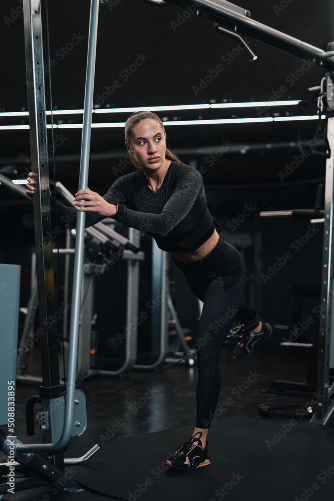 girl athlete shakes her legs on the simulator in the gym. dark background girl athlete shakes her legs on the simulator in the gym. dark background