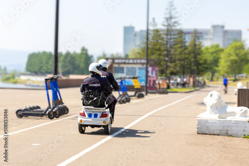 Police patrol on a mini scooter patrol the city embankment. Translation: Police. Panning shot
