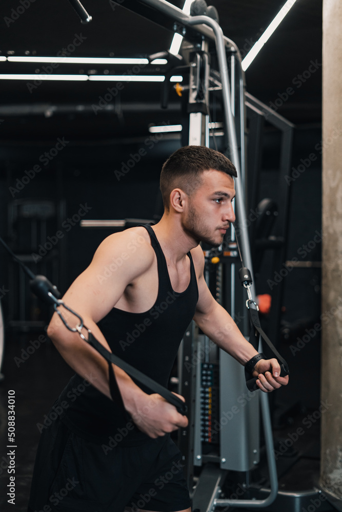 the guy pumps his chest on the simulator in the gym. dark background the guy pumps his chest on the simulator in the gym. dark background