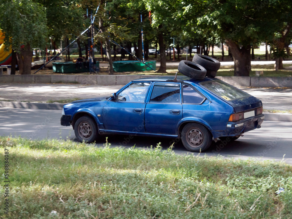 Provident disabled person driving an old car. He placed three spare tires on the roof of the car. Provident disabled person driving an old car. He placed three spare tires on the roof of the car.