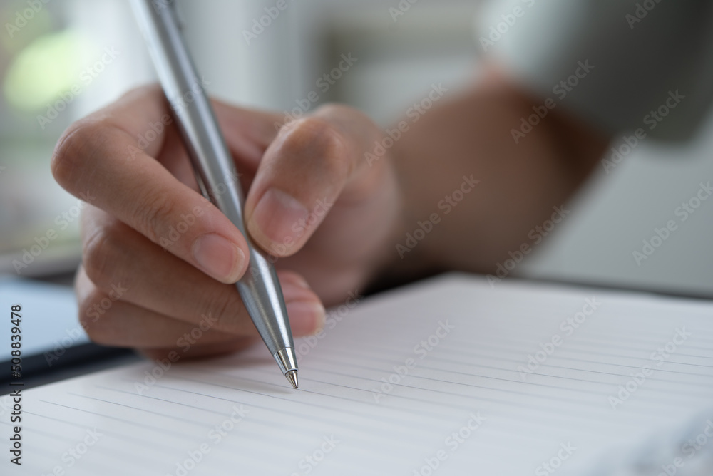 Close up of business woman hand with a pen writing note on spiral notepad on office table Close up of business woman hand with a pen writing note on spiral notepad on office table