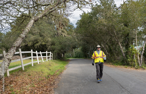 Man walking along a rural country road wearing a safety vest for visibility.