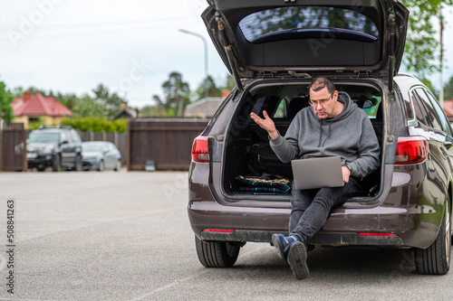a man sitting in the open trunk of a car and working with a laptop, mobile technology, remote work © ako-photography