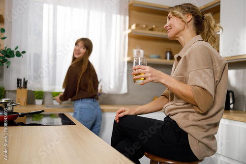 Mother relaxing enjoying apple juice while her daughter washes dishes in the kitchen