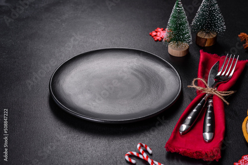Christmas table setting with empty black ceramic plate, fir tree and black accessories