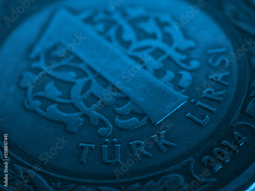 Translation: Turkish lira. Fragment of Turkish 1 one lira coin close-up. National currency of Turkey. Blue tinted money background. Backdrop for news about economy or finance. Macro photo