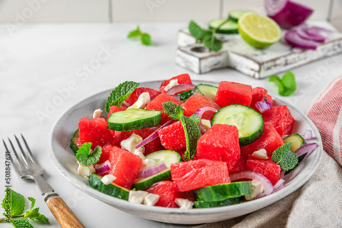 Summer salad with watermelon, cucumber, cheese and mint in a plate on white table with fork. close u