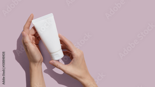 Young female hands holding blank white squeeze bottle plastic tube on pink background. Packaging of cream, lotion, gel, facial foam or skincare. Cosmetic beauty product branding mock-up. Copy space photo