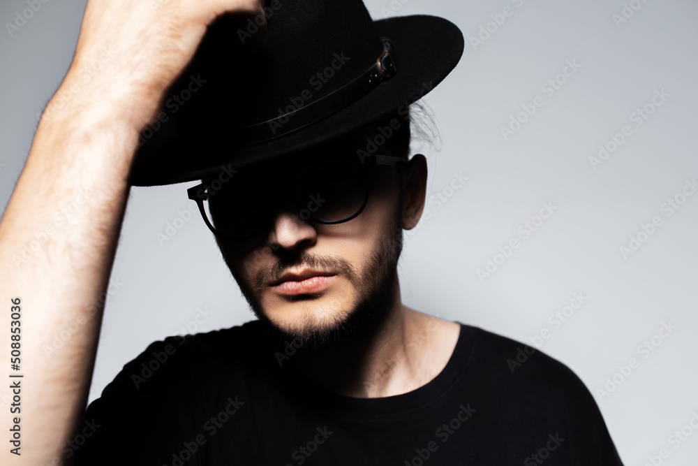 Close-up portrait of young handsome man wearing black hat and glasses on grey. Close-up portrait of young handsome man wearing black hat and glasses on grey.