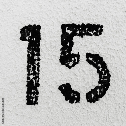Close-up of black painted number of 15 on background of grey textured wall.