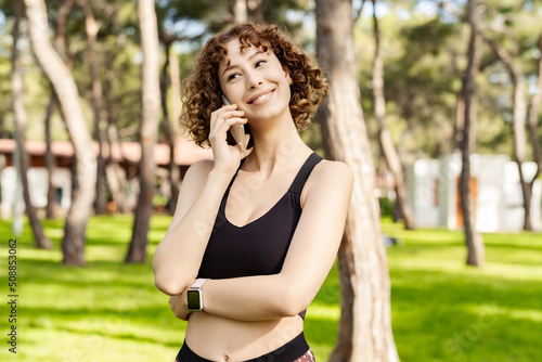 Quadro em tela Young beautiful woman wearing sportive clothes on city park, outdoors talking on mobile phone with friends or boyfriend with smiles