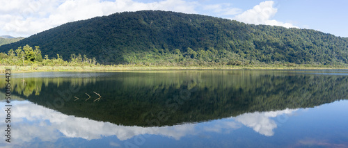 Stunning reflection of bush-clad mountains in calm surface of Lake Moeraki