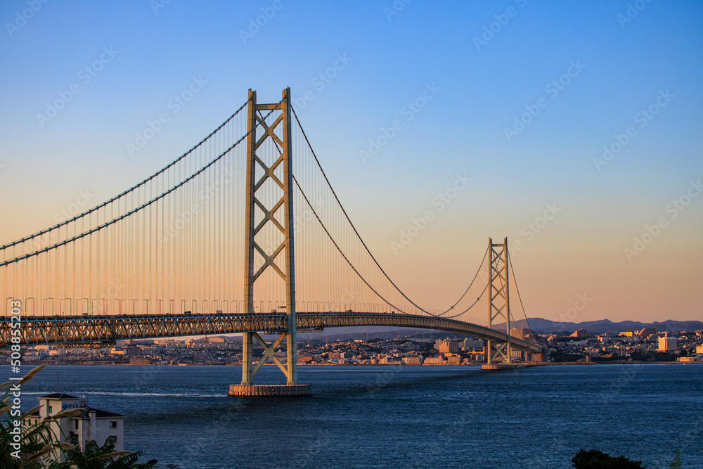 Towering suspension bridge over calm channel at sunset Towering suspension bridge over calm channel at sunset