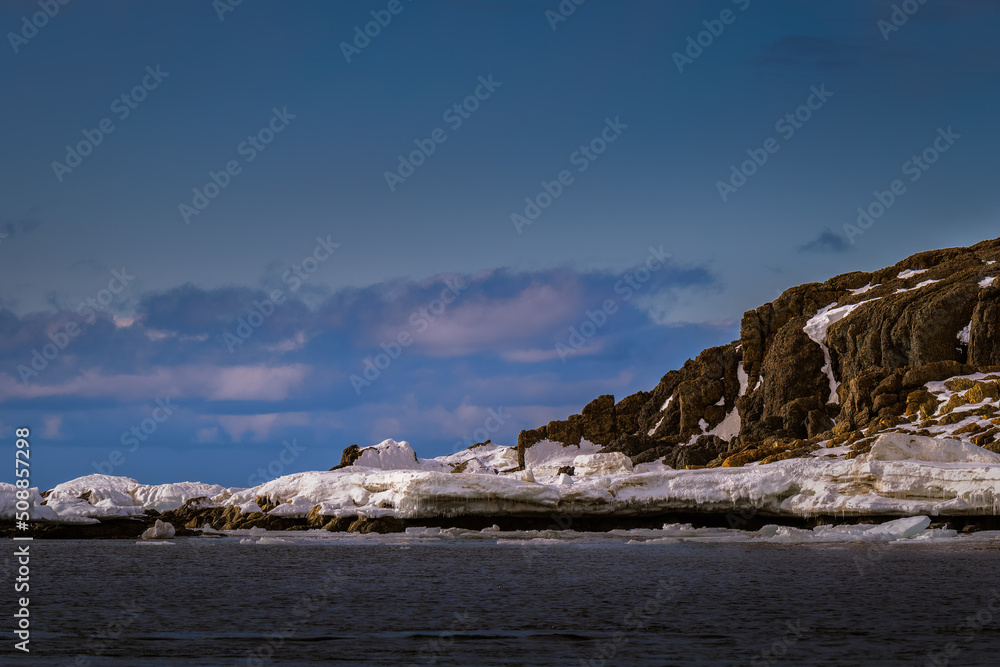 2022-05-16 A ROCK STRUCTURE PARTIALLY COVERED IN ICE IN THE ARCTIC NEAR THE ISLAND OF SVALBARD NORWAY WITH A NICE BLUE TINTED SKY