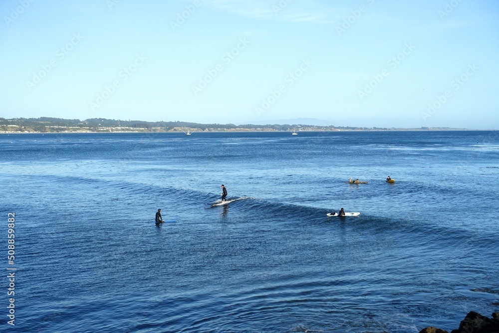 People enjoying a beautiful evening surfing in Monterey Bay, along the beachfront of Capitola, California, United States