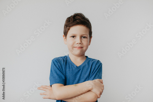 A preschool boy in a blue T-shirt on a light background shows a thumbs up