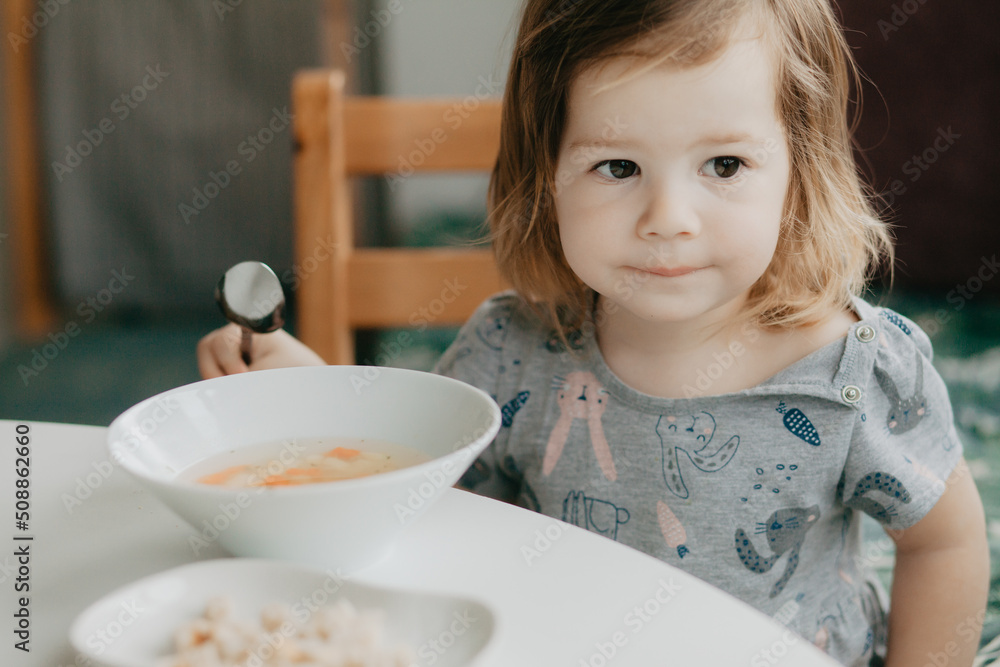 a little girl is sitting at the kitchen table eating soup a little girl is sitting at the kitchen table eating soup