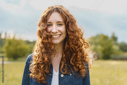 Spontaneous pretty young redhead woman smiling looking at the camera outdoors in the nature - portrait of a red head girl in the countryside photo