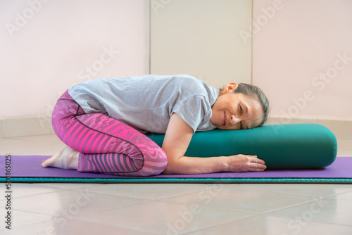 Foto Full length shot of energetic mature woman making exercising and practicing restorative yoga on mat and bolster at home because of social distancing, wearing sports clothes