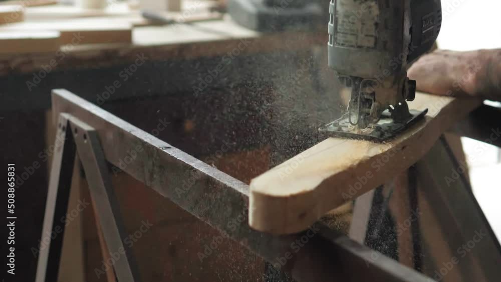 Close-up, a carpenter in his workshop saws a wooden board with an electric jigsaw, makes furniture parts in natural light. Woodwork.Slow-motion Carpenter saws wood, processing it. Home renovation Close-up, a carpenter in his workshop saws a wooden board with an electric jigsaw, makes furniture parts in natural light. Woodwork.Slow-motion Carpenter saws wood, processing it. Home renovation