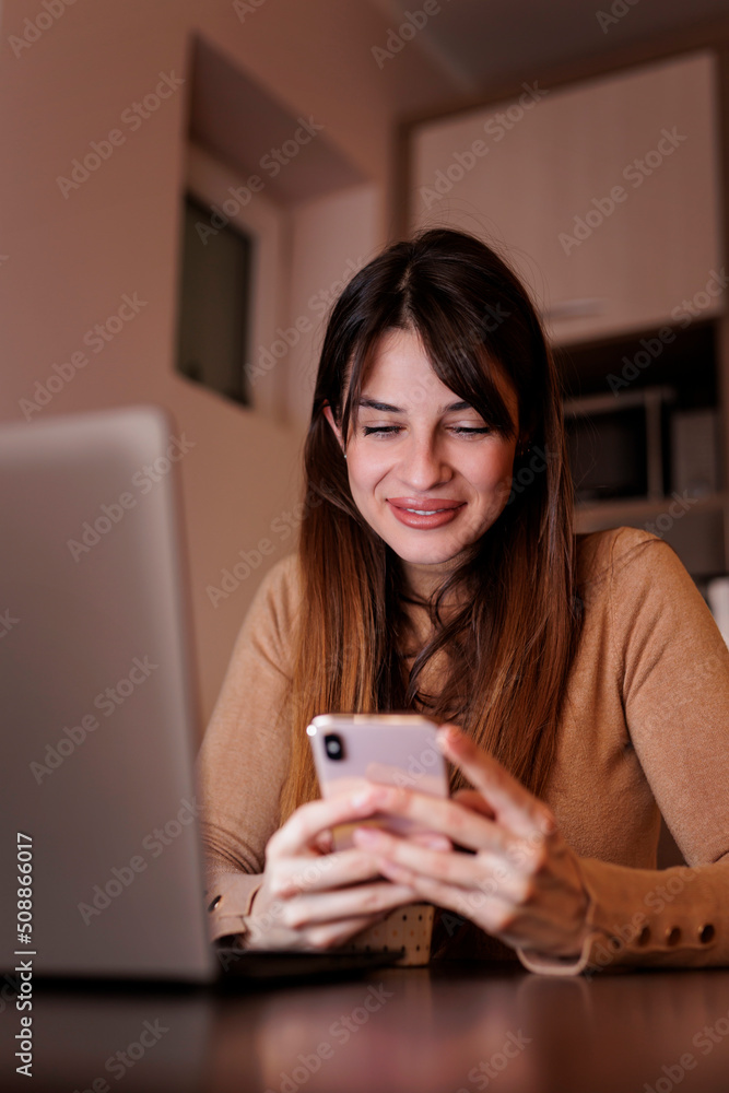 Female freelancer using smart phone while working late in home office Female freelancer using smart phone while working late in home office