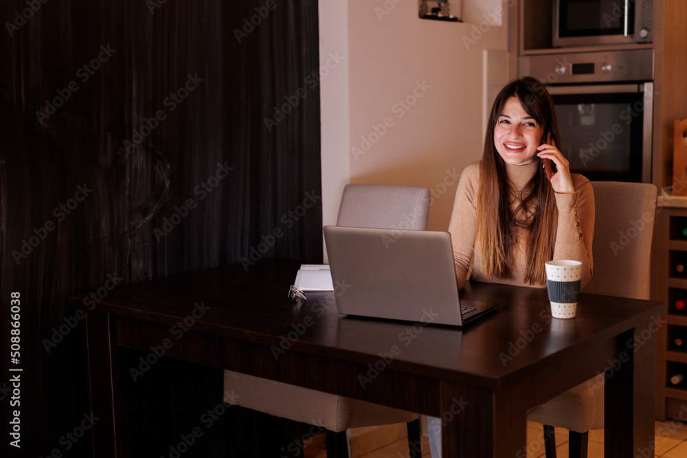 Woman having phone conversation while working late from home Woman having phone conversation while working late from home