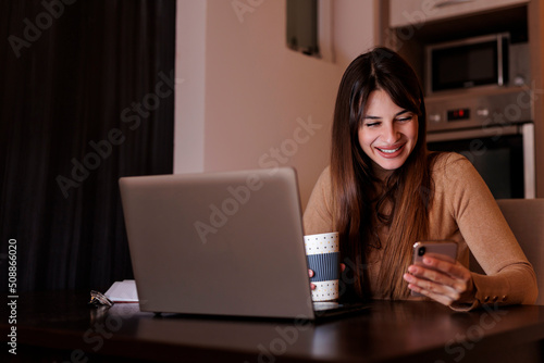 Freelancer drinking coffee and using smart phone while working remotely from home