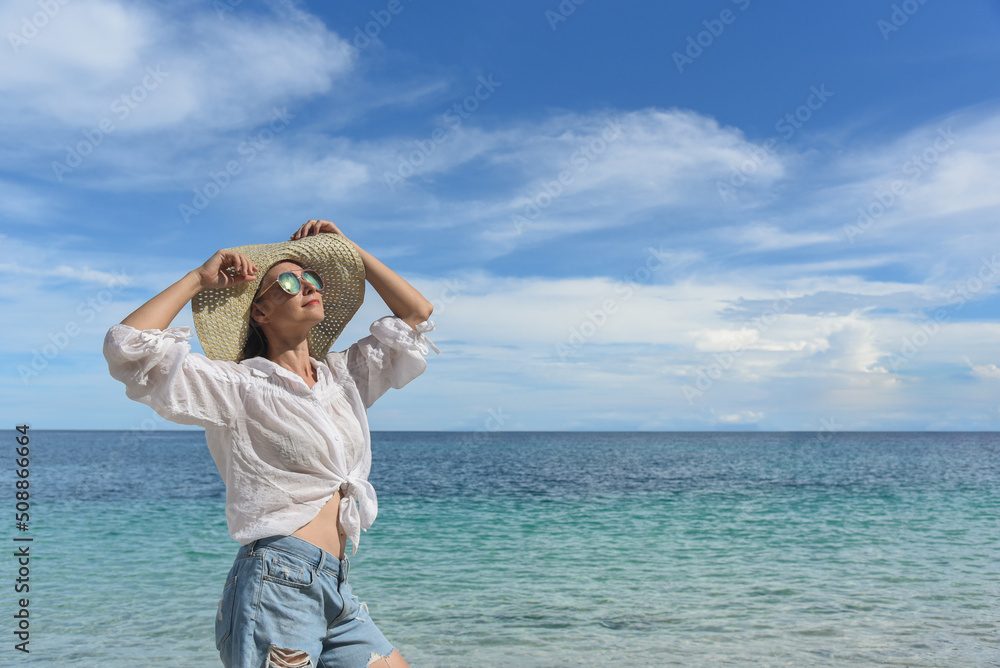 A woman is resting on the beach. She is wearing a straw hat, denim shorts and a white shirt. Travel and good rest, happy holidays, tourism, Philippines, summer season. Side view, copy space