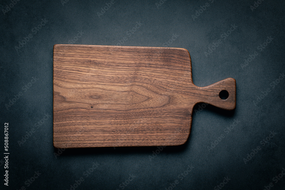 A handcrafted black walnut wood chopping board sits on a dark-toned tabletop. walnut wood board. - obrazy, fototapety, plakaty 