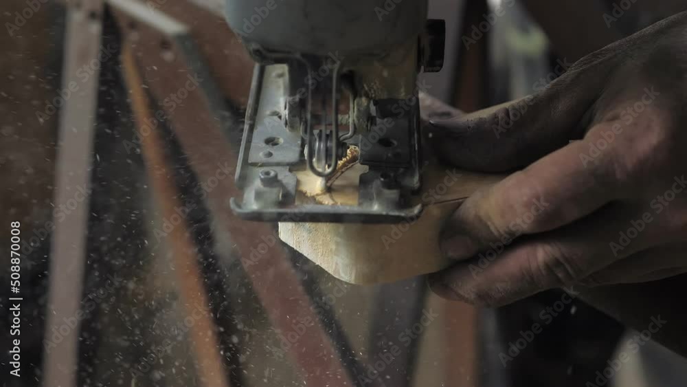 Close-up: a carpenter in his workshop saws a wooden board with an electric jigsaw, makes furniture parts in natural light. A carpenter works with wood, processing it.Construction Tools For Home Repair Close-up: a carpenter in his workshop saws a wooden board with an electric jigsaw, makes furniture parts in natural light. A carpenter works with wood, processing it.Construction Tools For Home Repair