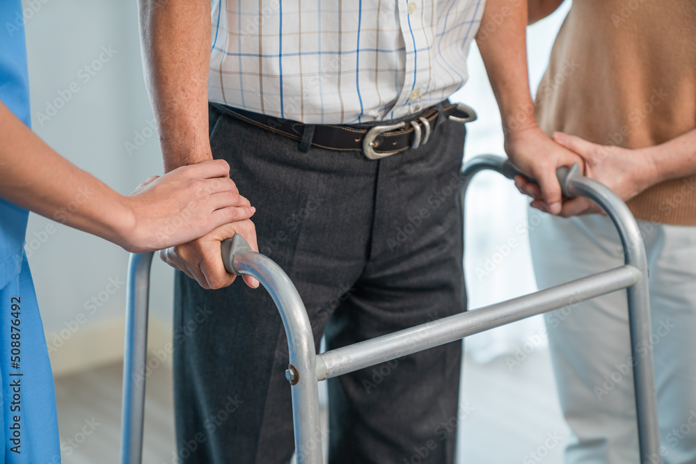 Closeup of elderly man's hands holding walker practice walking with supporting caregiver nurse woman helping him during home visit