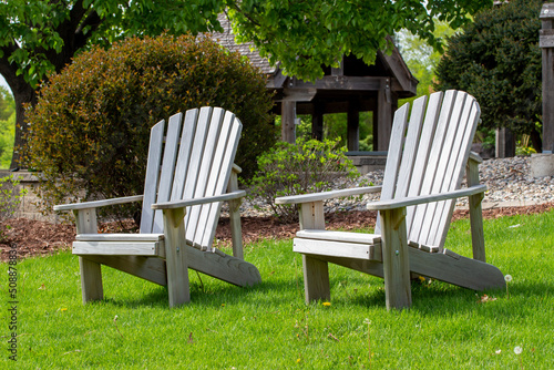 Close up view of a pair of wooden adirondack chairs on a landscaped grass lawn on a sunny day 