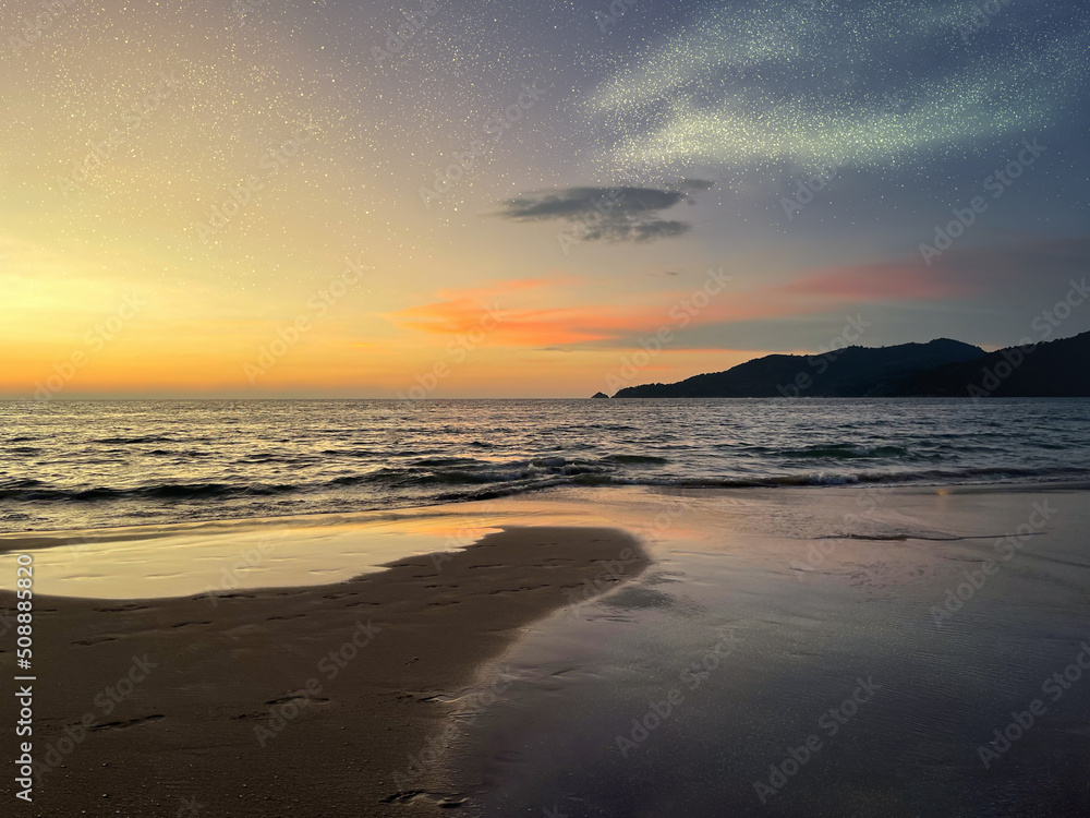 Beautiful panoramic view of sea, deserted beach and cape covered with forest. Seascape at sunset. Amazing skies with scattering of shining stars and bright orange yellow glow of setting sun on sky.