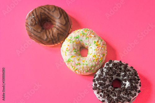 Colorful glazed donuts isolated on a pink background. Set of three different doughnuts. Flat lay. Top view.