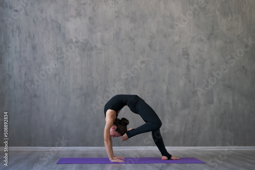 Athletic young woman practice yoga down, face down isolated on gray wall background in black sportswear. Concept healthy lifestyle and natural balance between body and mental development. Full lengths