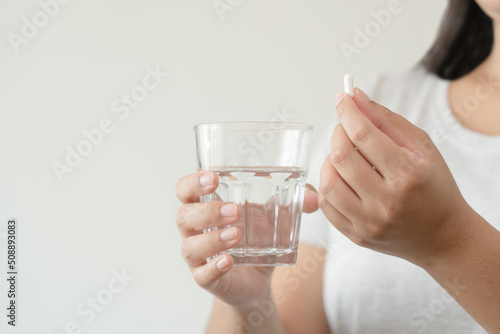 Asian woman close up ready to take supplement pill holding a glass of water. Sick person need medicine and water for good health.