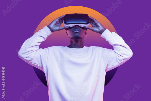 African american man looking up at virtual reality or metaverse in vr glasses isolated on purple