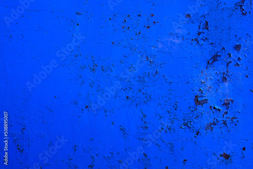 Bright blue background of a metal wall with cracks and rust.